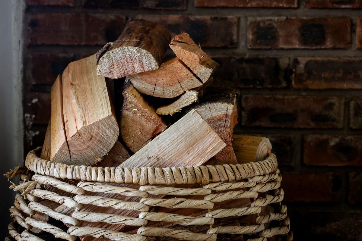 Firewood basket topped with a pumpkin and autumn leaves beside a hearth