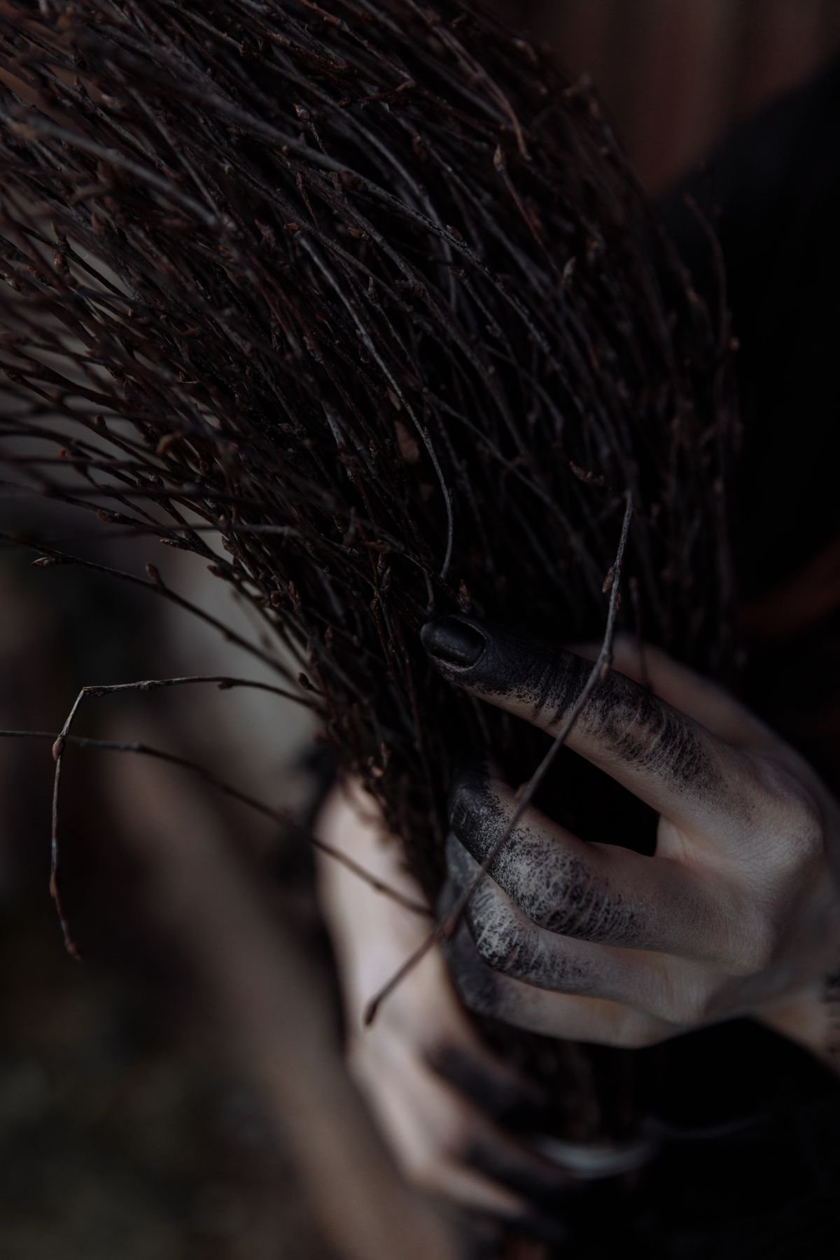 Witch hand gripping a twig broom, dark halloween garden detail