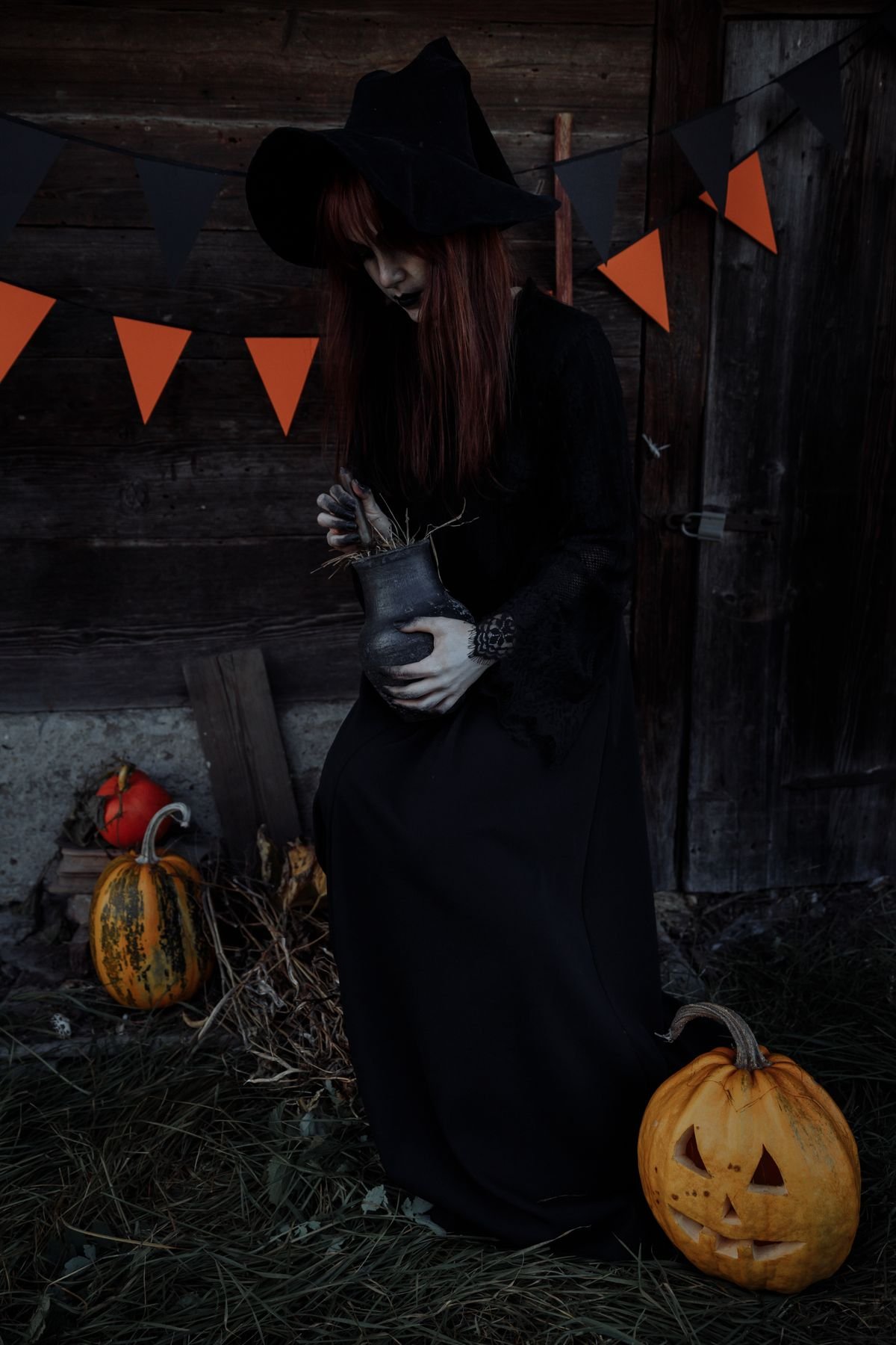 Witch standing beside a carved pumpkin with halloween bunting