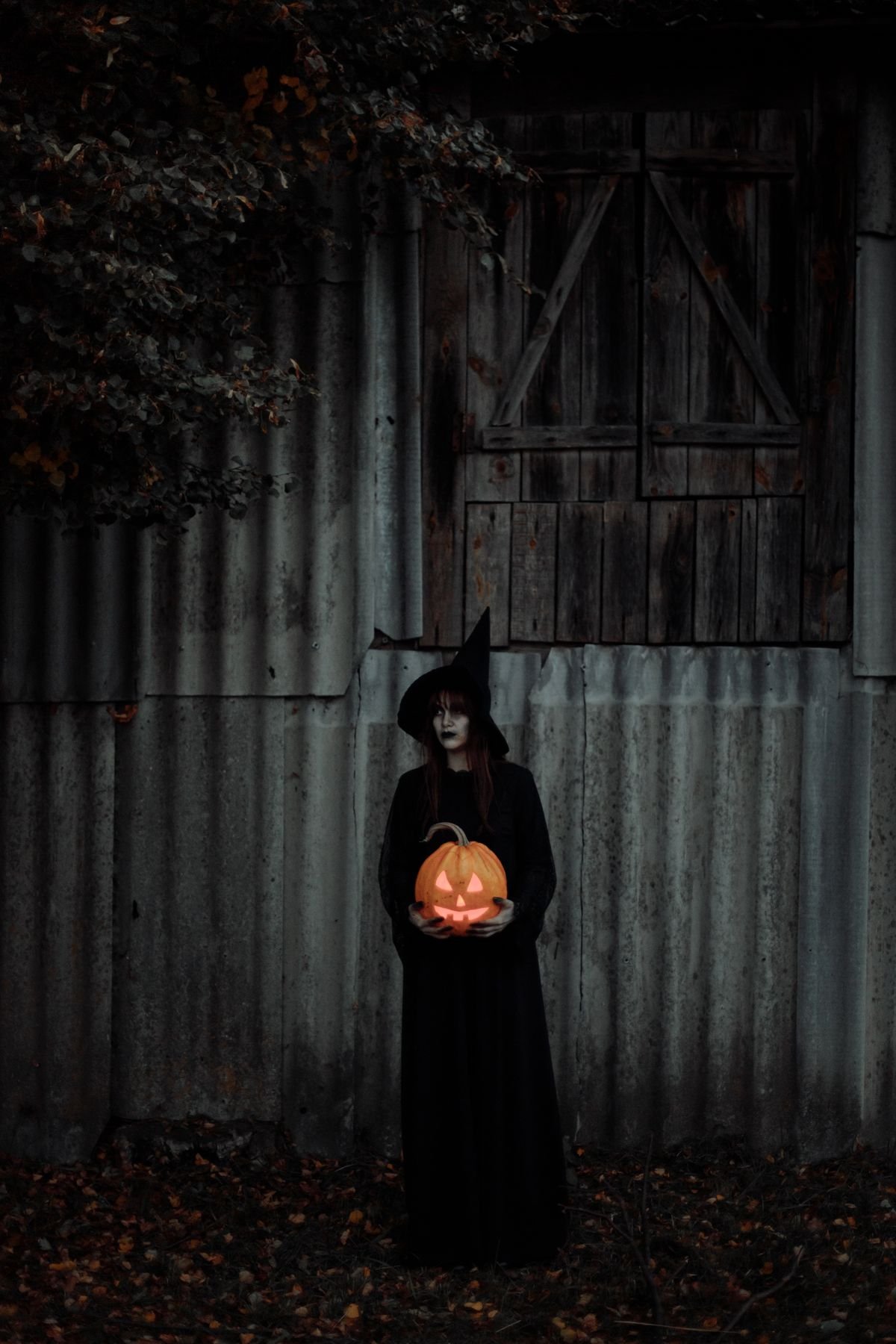 Witch holding a pumpkin in front of a dark metal door, spooky halloween entrance